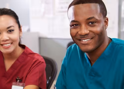 Medical students in differently-colored scrubs sit in a room.
