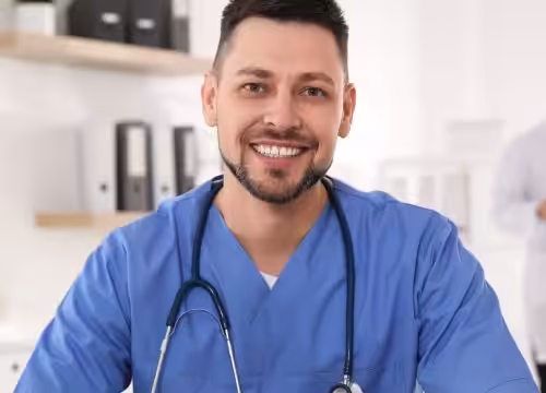 A male medical professional smiles at the camera, with another professional in the background.