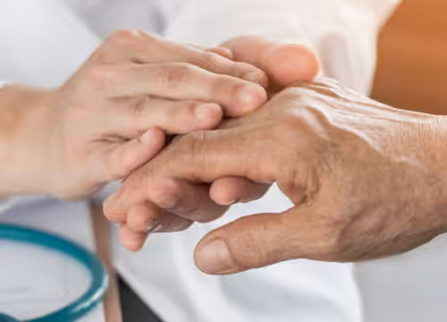 A medical professional's hands hold an elderly person's hand, with a stethoscope visible.