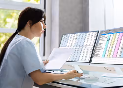 Woman in scrubs sitting in front of computer screens