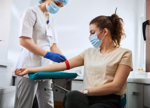 Skilled focused young phlebotomy technician applying a tourniquet to a female patient arm for venipuncture