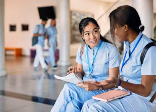 Asian nursing student and her female friend talk while studying in hallway at medical university.