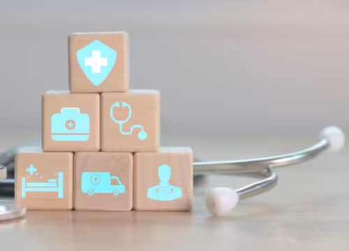 Six wooden blocks with health care icons are stacked on a table with a stethoscope.