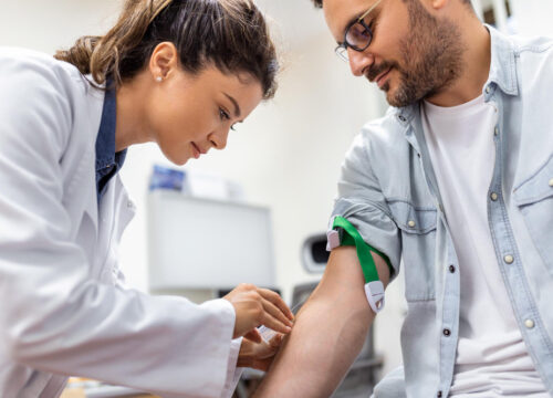 Phlebotomist applying a tourniquet and preparing to draw blood from a patient’s arm.